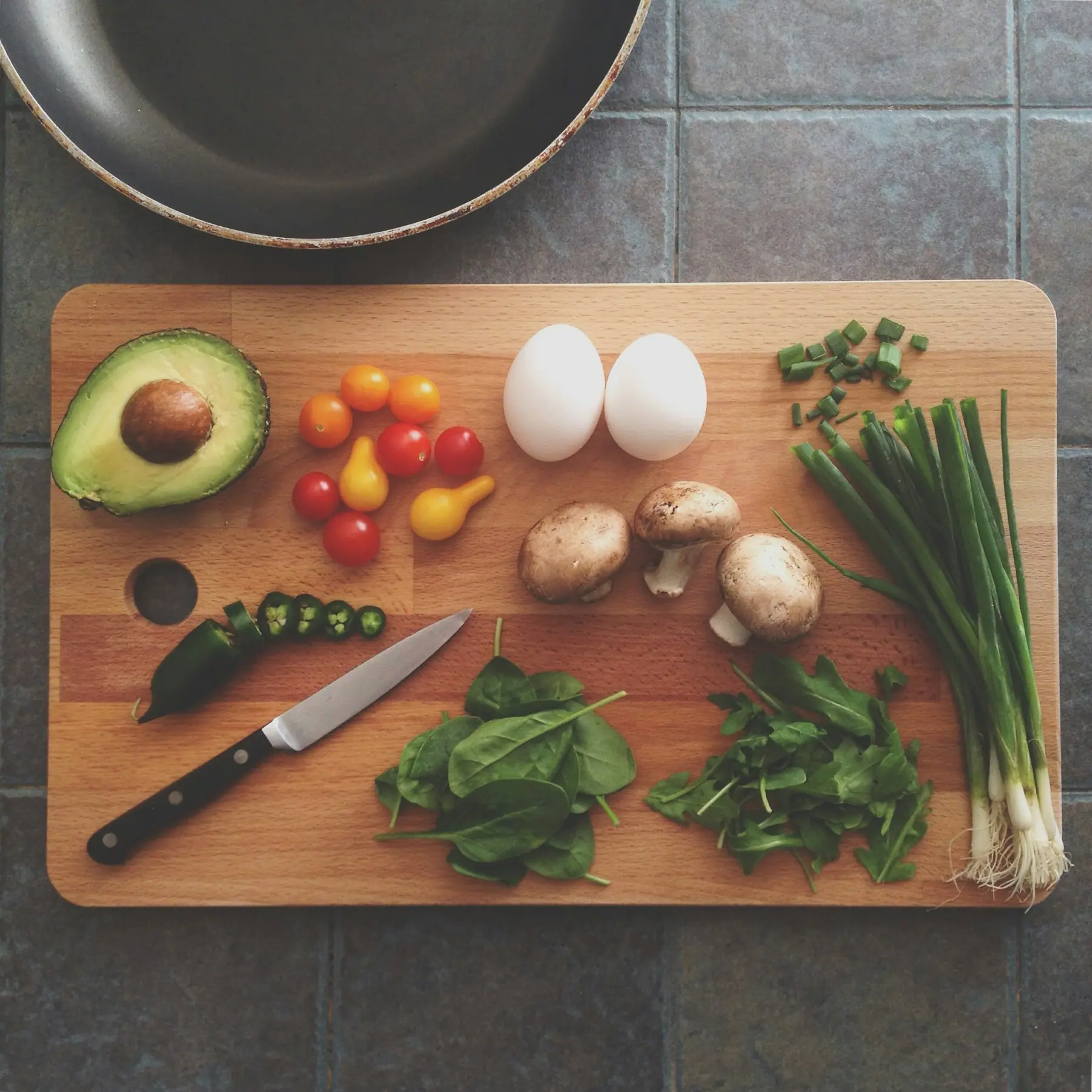 Avocado, eggs, tomatoes, mushrooms, scallions and herbs on a wooden cutting board