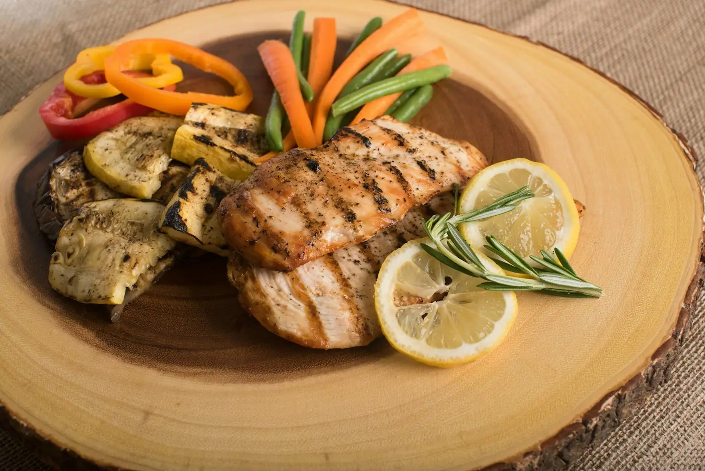 Grilled chicken breasts with lemon slices and roasted peppers on a wooden board